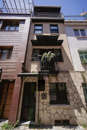 A multi-story building with a stone facade, a balcony with plants, and a door with a sign. - Mercan Apartments Balat (Fatih)