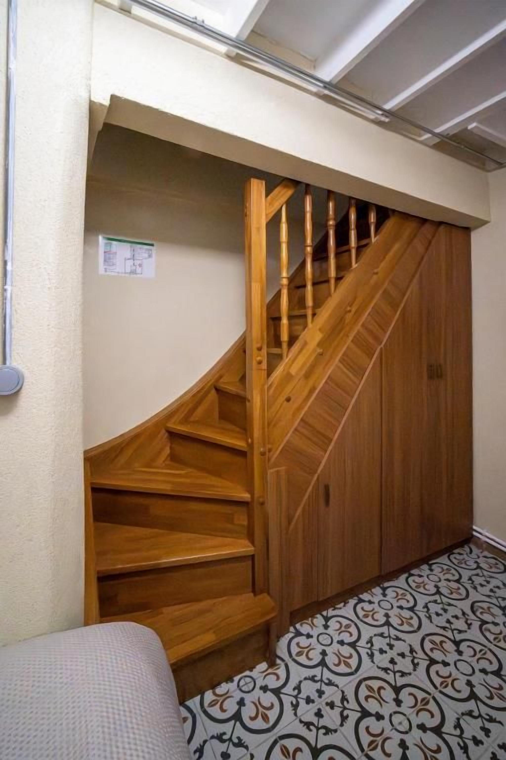 A wooden staircase leading to a closet with patterned flooring.