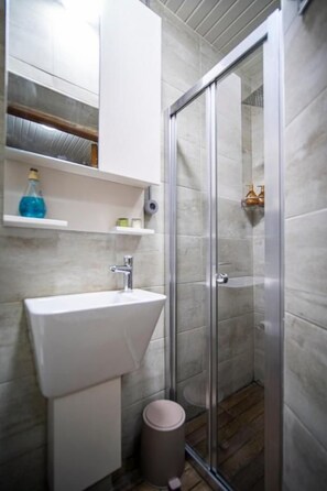 A bathroom with a white sink, a glass shower enclosure, and a trash bin. - Mercan Apartments Balat (Fatih)