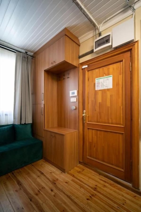 A room with a wooden floor, a green sofa, a wooden wardrobe, and a door with a notice.