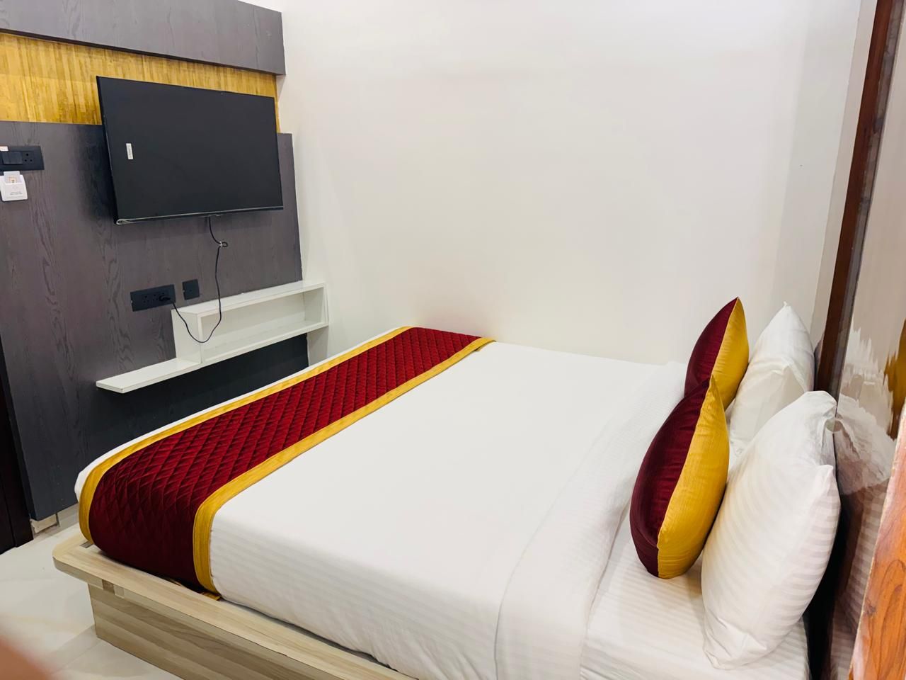 Habitación de hotel con cama, televisor montado en la pared y cabecero de madera.