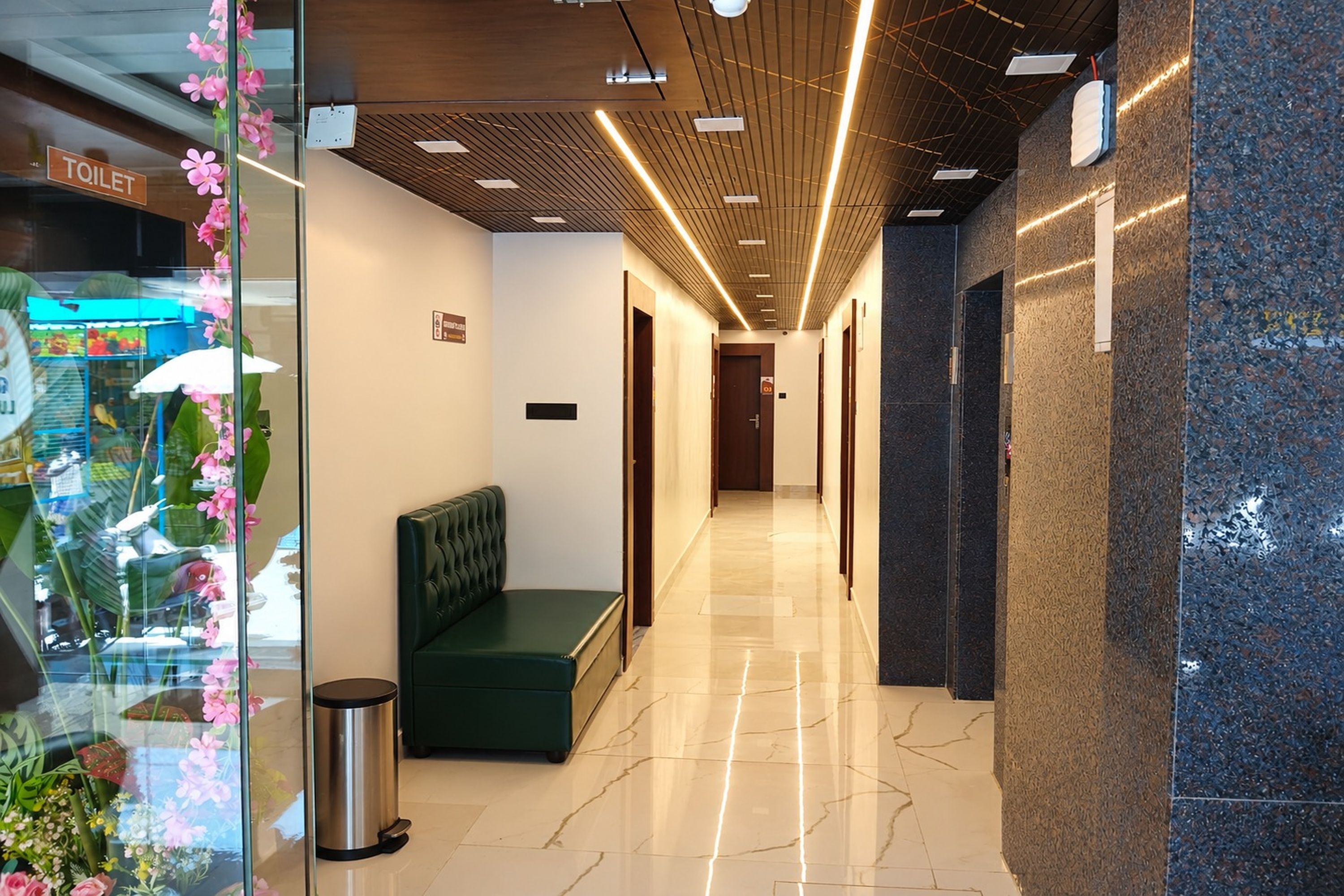 Pasillo de hotel con un banco, un bote de basura y una zona de recepción con techo y pared de madera.
