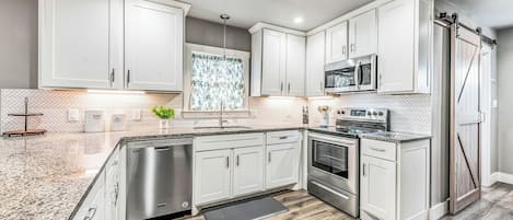 A modern kitchen with white cabinetry, stainless steel appliances, and a herringbone tile backsplash.