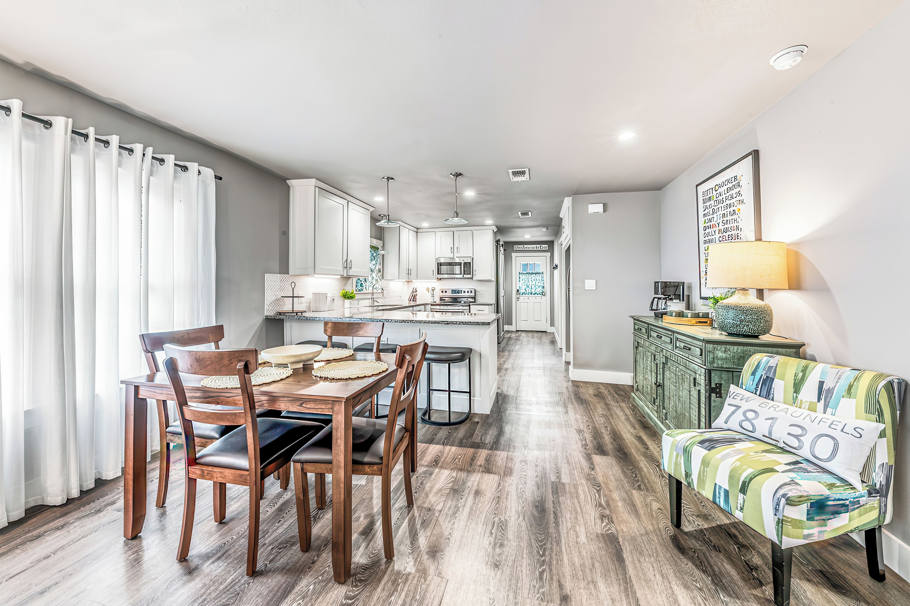 Una cocina moderna con armarios blancos, una zona de comedor con sillas de madera, y un sofá con un cojín que muestra el número 830.