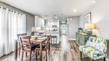 Una cocina moderna con armarios blancos, una zona de comedor con sillas de madera, y un sofá con un cojín que muestra el número 830.