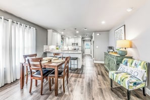 A modern kitchen with white cabinets, a dining area with wooden chairs, and a sofa with a cushion displaying the number 830.