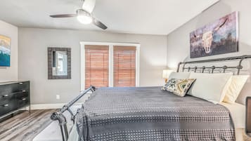 A bedroom with a bed, a ceiling fan, a window with blinds, a dresser, and a painting on the wall.