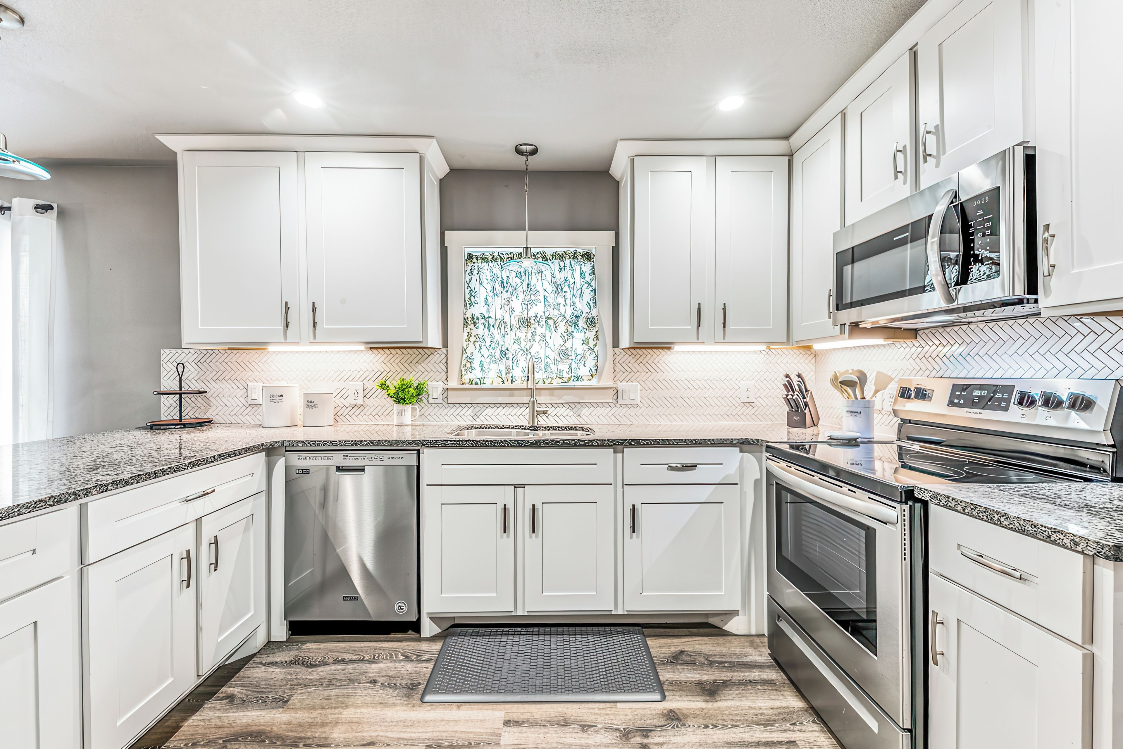 Une cuisine moderne avec des meubles blancs, des appareils en acier inoxydable et un dosseret de carrelage disposé en motif chevron.