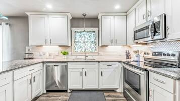 Une cuisine moderne avec des meubles blancs, des appareils en acier inoxydable et un dosseret de carrelage disposé en motif chevron.