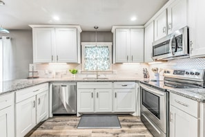 A modern kitchen with white cabinetry, stainless steel appliances, and a herringbone tile backsplash.