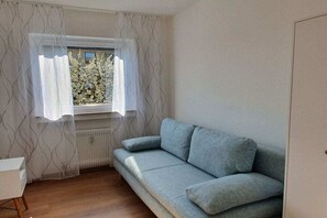 A room with a light blue sofa, a radiator, and a window with sheer curtains. - Holiday apartment with 2 bedrooms (Gaienhofen-Horn)