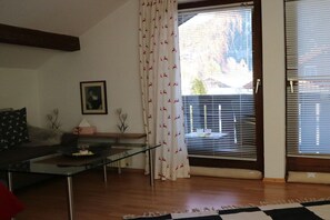A living room with a glass coffee table, a sofa, a picture on the wall, and a window with blinds. - 3 - Nina's Country House (Hohenschwangau)