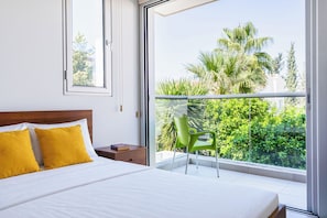 A bedroom with a bed, a nightstand, a green chair, and a balcony with a view of greenery. - Modern Elegant UNIC Studio Suite (Egkomi Lefkosias)