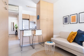 A modern living room with a sofa, a coffee table, and a kitchen area with a refrigerator and cabinets. - Modern Elegant UNIC Studio Suite (Egkomi Lefkosias)
