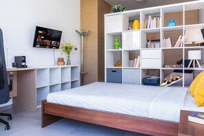 A modern hotel room with a wooden bed, a desk with a coffee maker, a TV mounted on the wall, and a large white shelving unit with various items. - Modern Elegant UNIC Studio Suite (Egkomi Lefkosias)