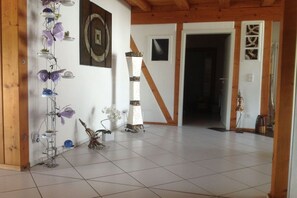 A room with a tiled floor, a wooden ceiling, and a door leading to another room. There are decorative items on a stand and a plant on the floor. - Exclusive holiday home with pool (Berghaupten)