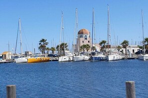 A marina with multiple sailboats docked, a prominent building with a dome, and palm trees in the background. - Holiday home in Gruissan with swimming pool (Gruissan)