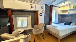 A hotel room with a bed, a chair, a small table, a window, and a wall clock. - Room Porcelaine Chambéry (Chambéry)