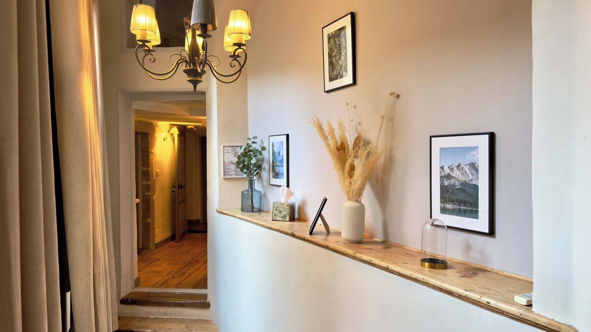 Um corredor com balcão de atendimento de madeira, quadros decorativos, um vaso com plantas secas e um candelabro.