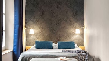 Un dormitorio con cama, dos lámparas de noche, una ventana con cortinas y un papel tapiz estampado.