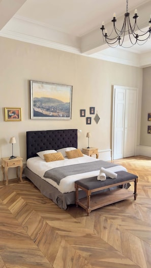 Een slaapkamer met een groot bed, een kroonluchter, een schilderij en een houten vloer.