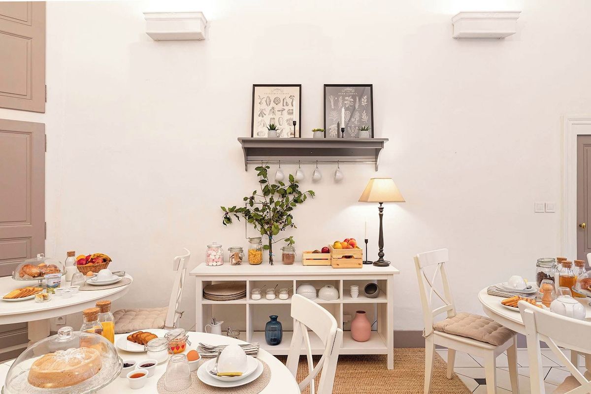 Een eetgedeelte met een ronde tafel, stoelen, een buffet en een wandplank met decoratieve objecten.