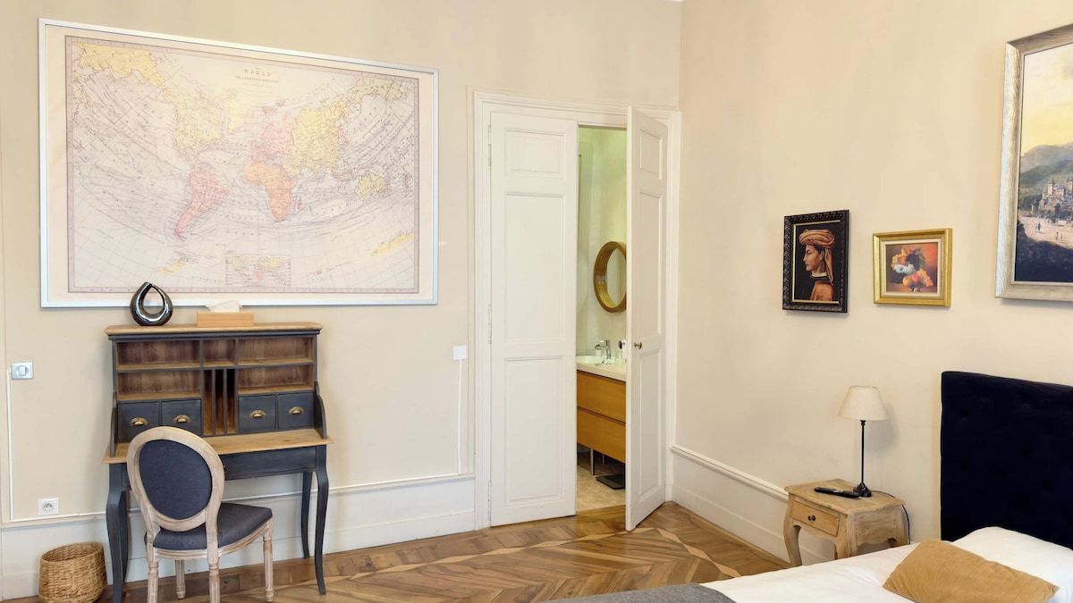 Una stanza con un letto, una scrivania con cassetti, una sedia, una mappa appesa al muro e una porta che dà sul bagno.