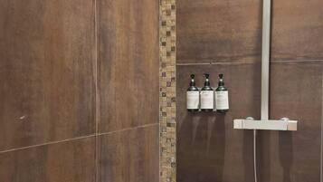 Een douchegedeelte met een betegelde muur, een douchekop en drie flessen shampoo.