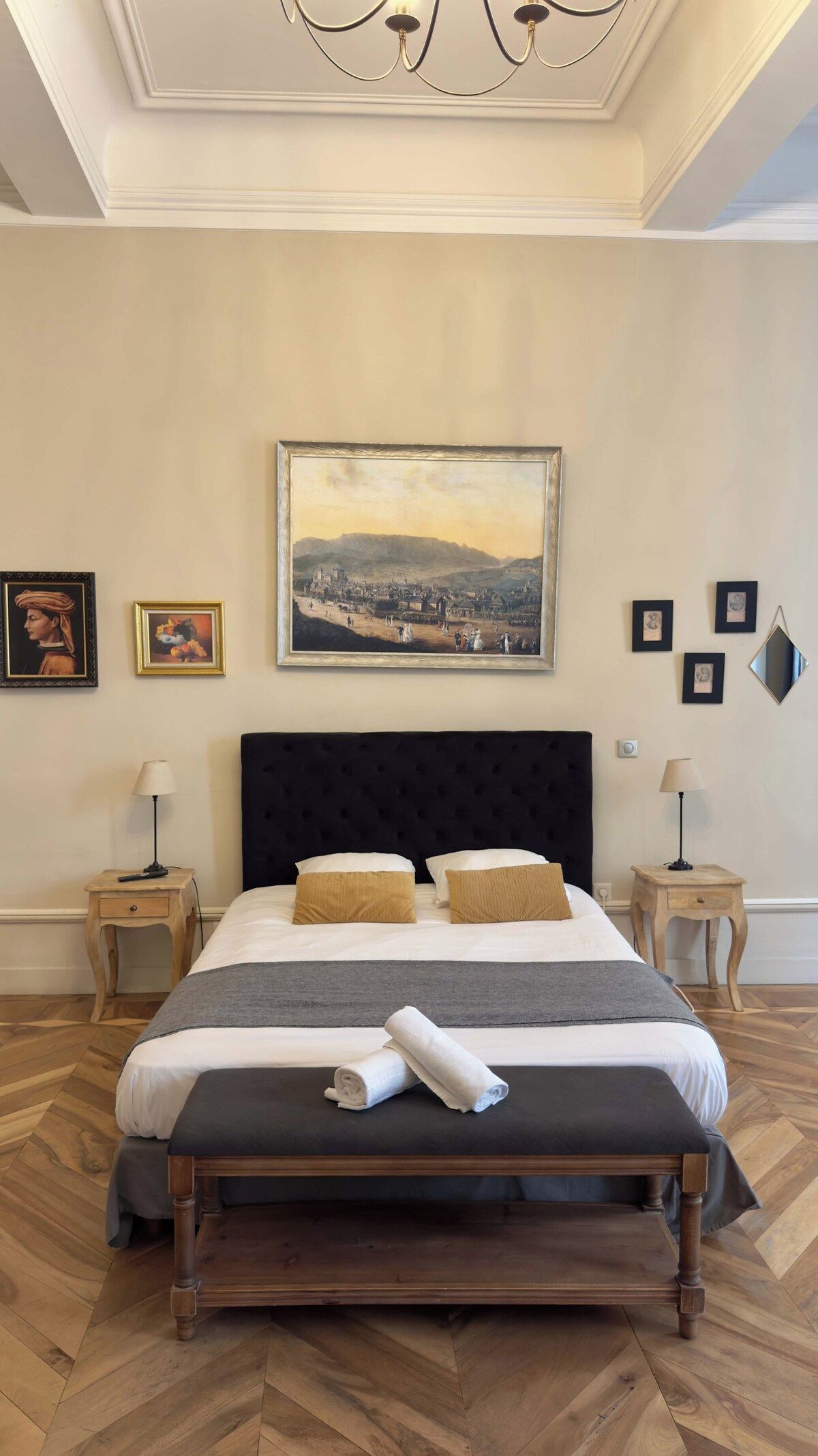 A hotel room with a large bed, a painting on the wall, and a chandelier.