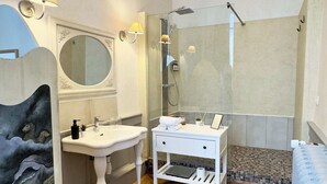 Bany amb un lavabo blanc, un mirall i una dutxa. Hi ha un penjador sobre el lavabo i un quadre a la paret.