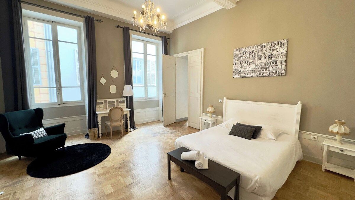 A bedroom with a large bed, a chair, a desk, and a window.