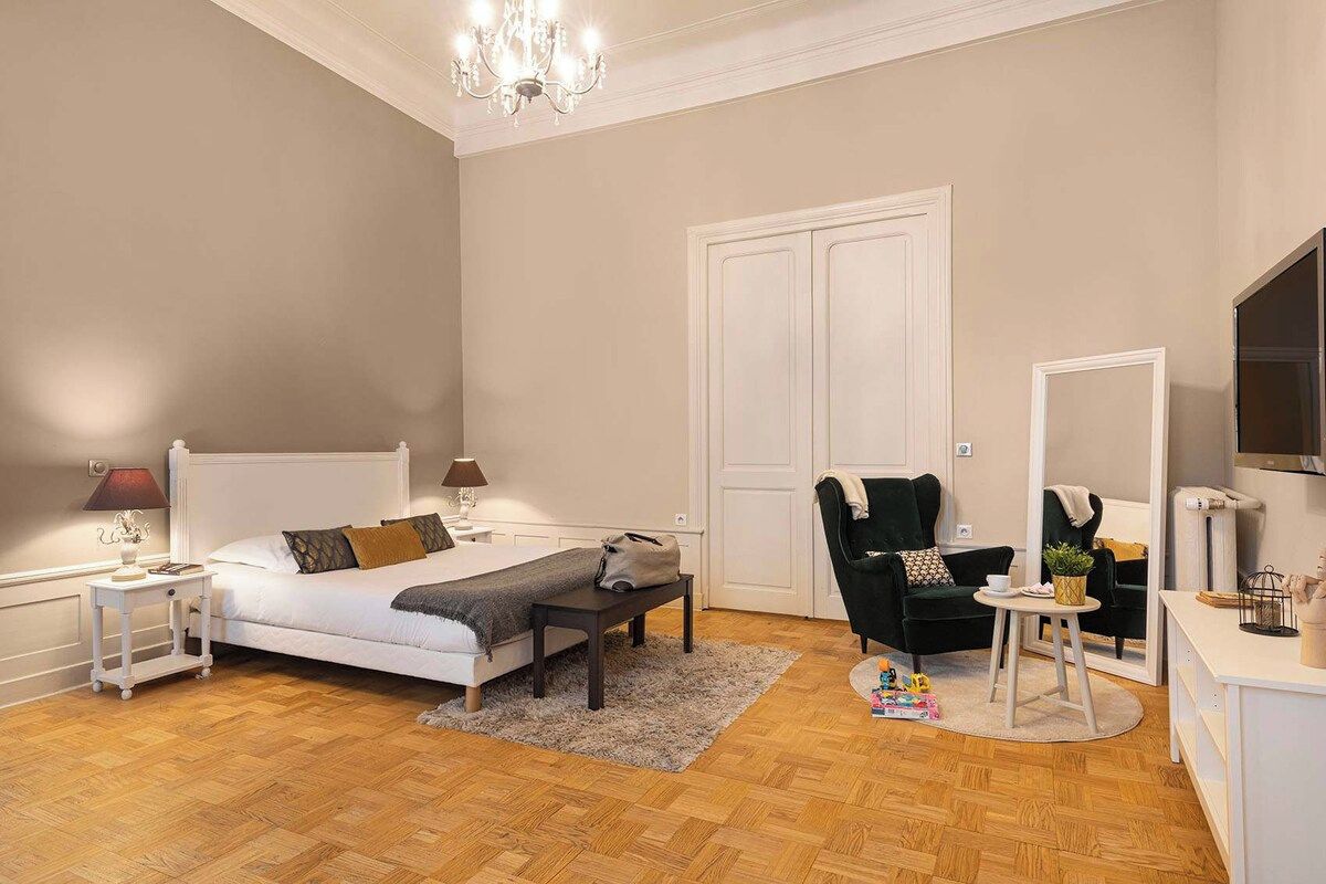 Un dormitorio con cama, mesitas de noche, una silla, escritorio y espejo.