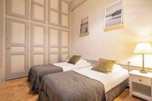 Een slaapkamer met twee bedden, een nachtkastje met een lamp en een deur met paneeldecoratie.