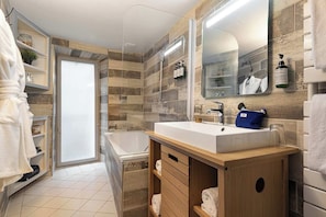 A modern bathroom with a large mirror, a bathtub, and a vanity with a sink. - Chambre Verveine Chambéry (Chambéry)
