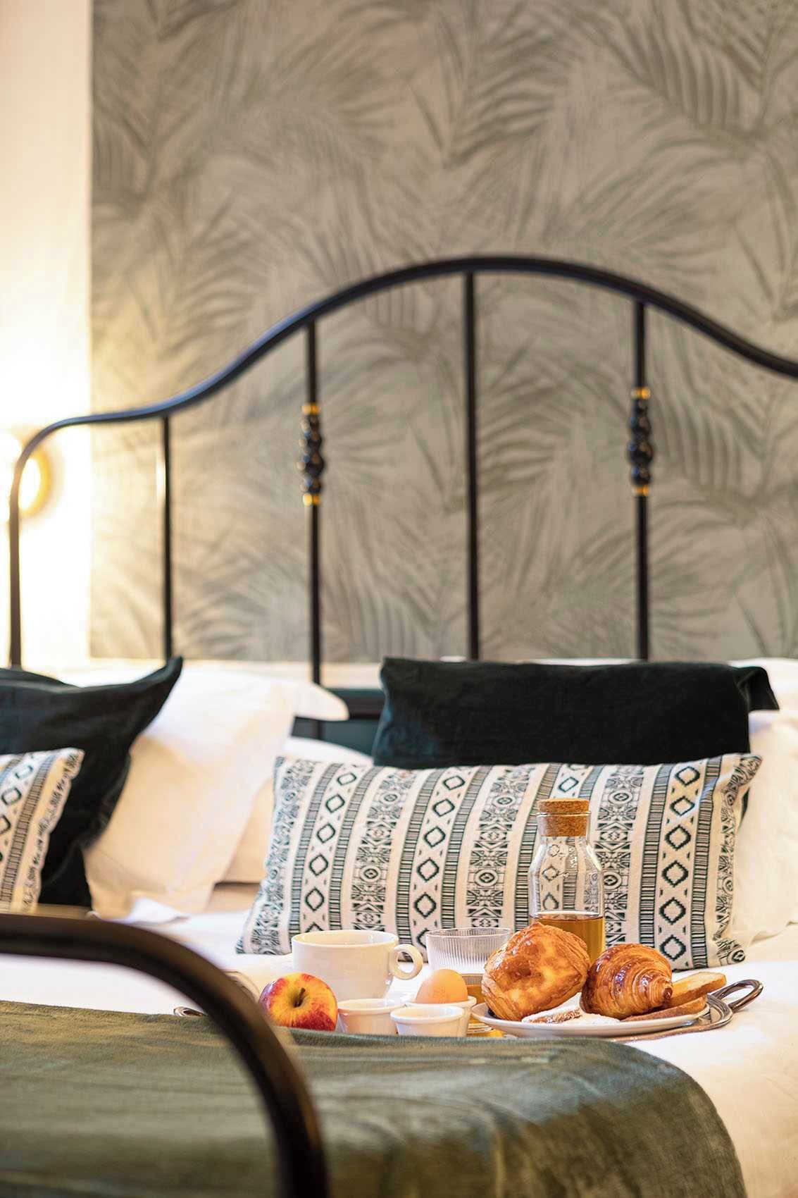 A neatly made bed with patterned pillows, a tray of croissants, and a bottle of water.