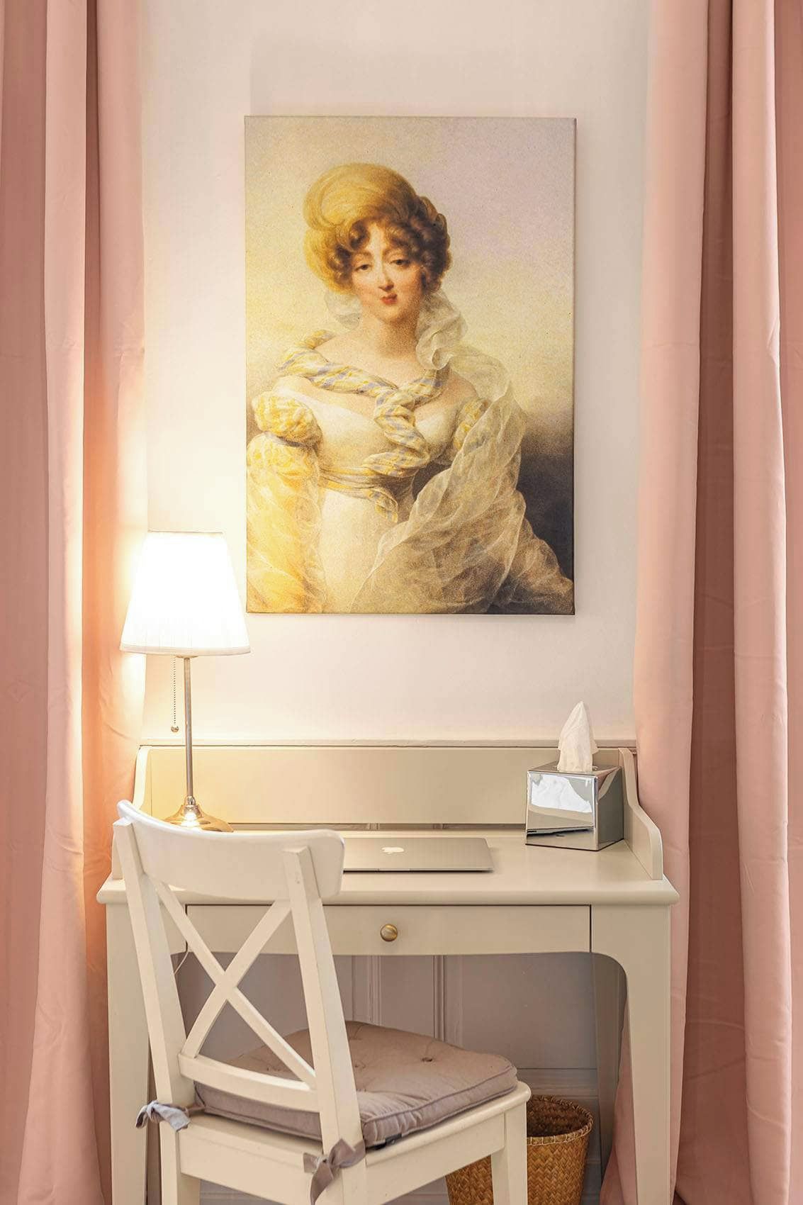 Quarto com escrivaninha, cadeira, luminária, caixa de lenços de papel e quadro na parede.
