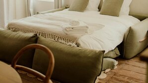 Een slaapkamer met een bed, kussens, een deken, een stoel en een raam.