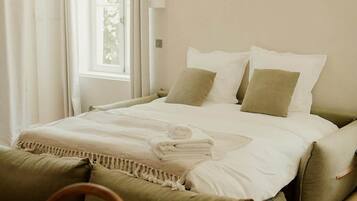 Een slaapkamer met een bed, kussens, een deken, een stoel en een raam.