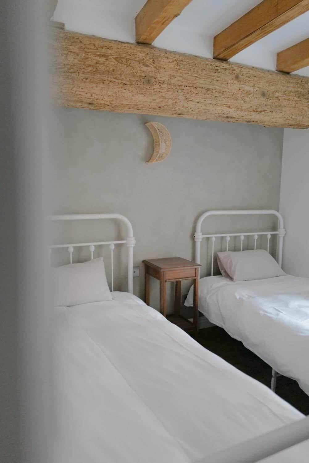 Een slaapkamer met twee bedden, een klein houten nachtkastje en een balken plafond.