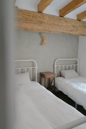 Een slaapkamer met twee bedden, een klein houten nachtkastje en een balken plafond.