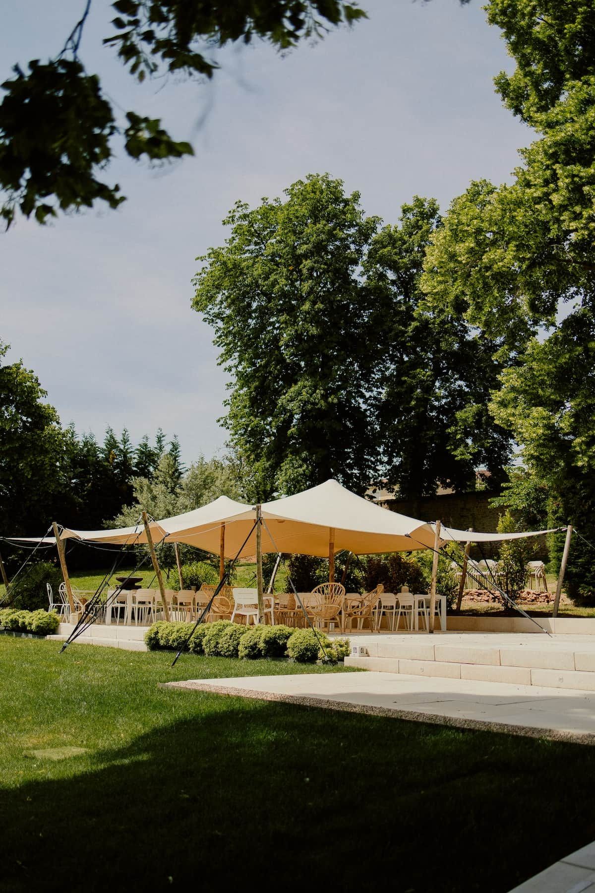 Een terras met overkapping, omringd door groen en bomen.