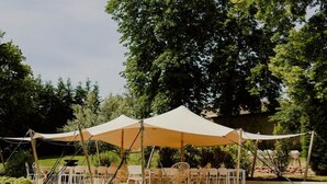 Een terras met overkapping, omringd door groen en bomen.