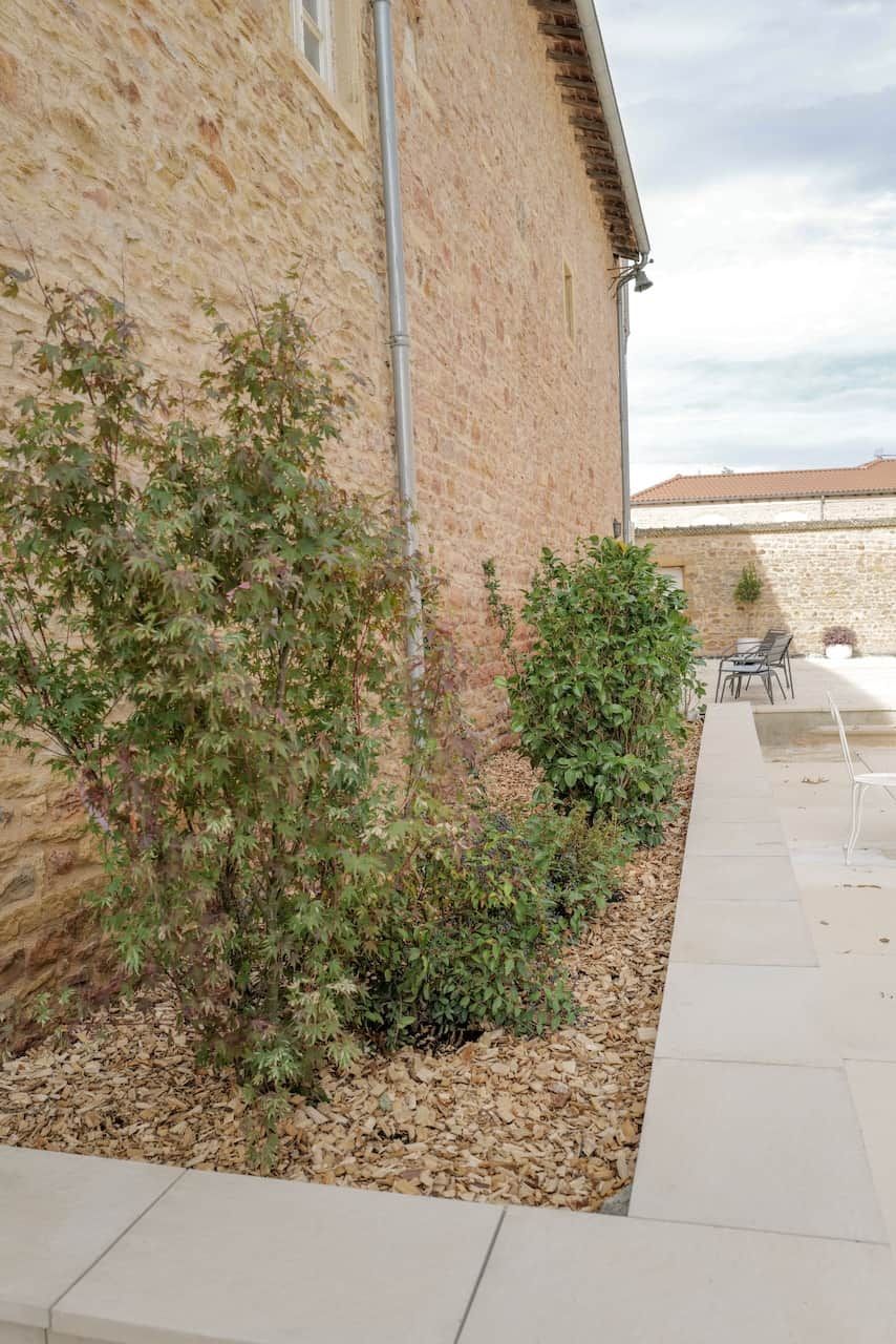 A stone building with a patio area, outdoor seating, and a small garden with shrubs.