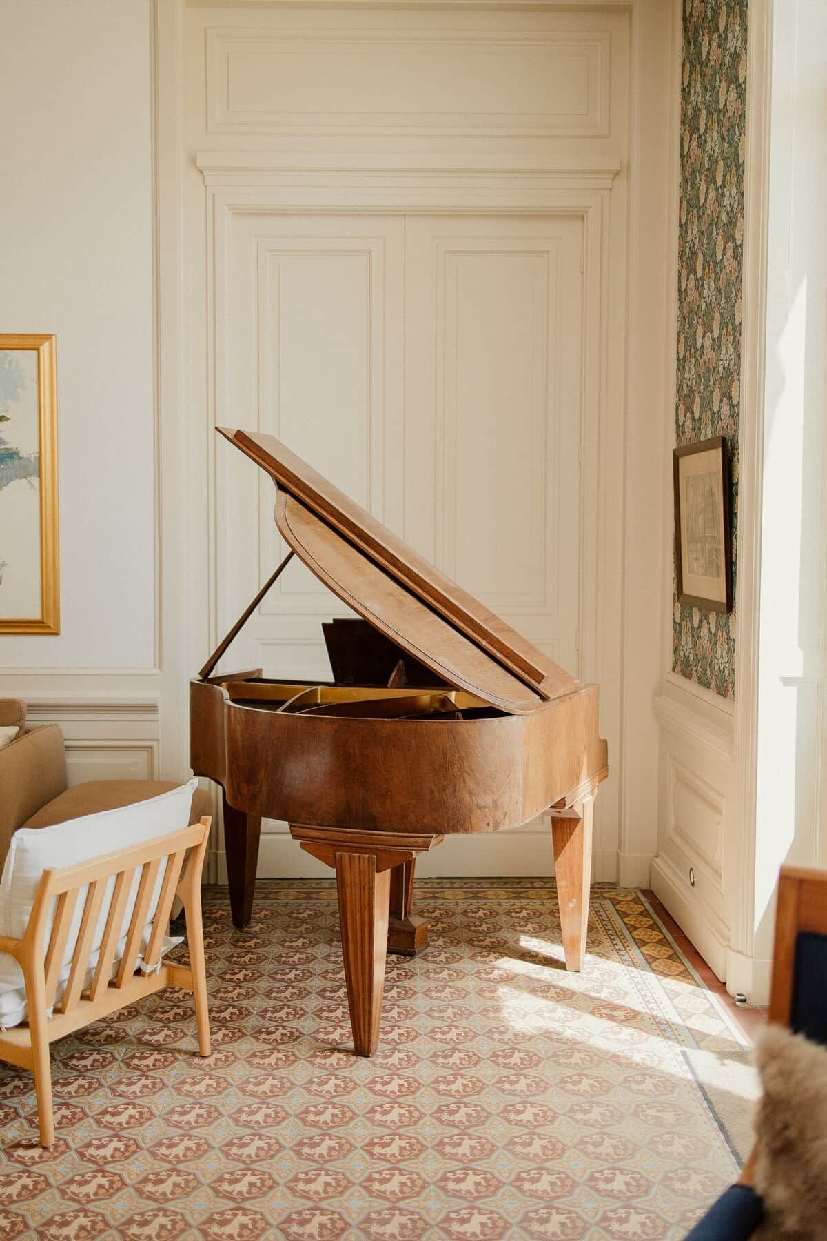 A grand piano in a room with patterned floor tiles, a wooden bench, and a white door with paneling.
