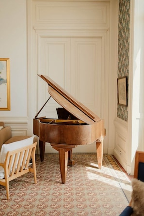 A grand piano in a room with patterned floor tiles, a wooden bench, and a white door with paneling.
