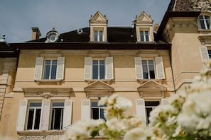 A multi-story building with symmetrical architecture, featuring a central entrance with a decorative pediment, multiple windows with shutters, and a balcony on the upper floor.