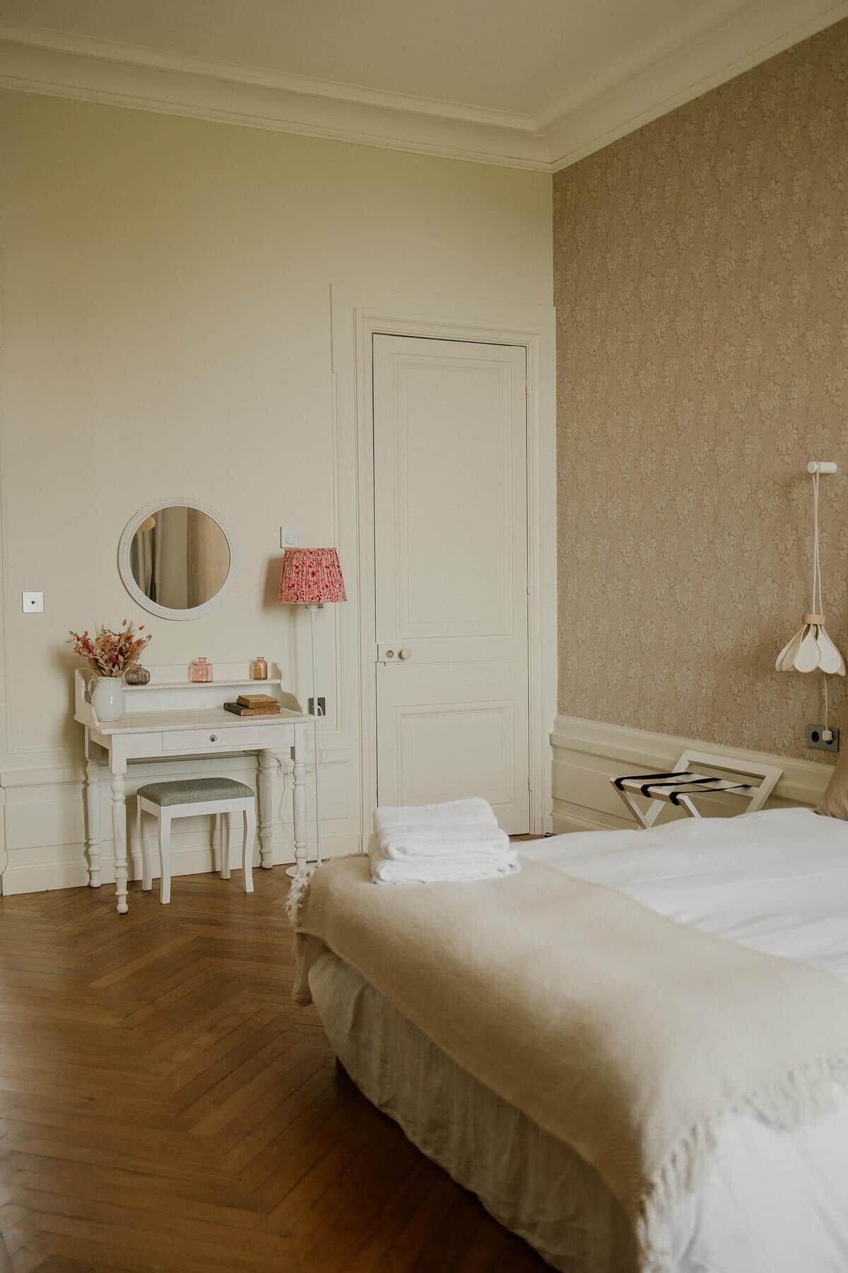 A bedroom with a bed, a bedside table, a mirror, a dresser, and a door.