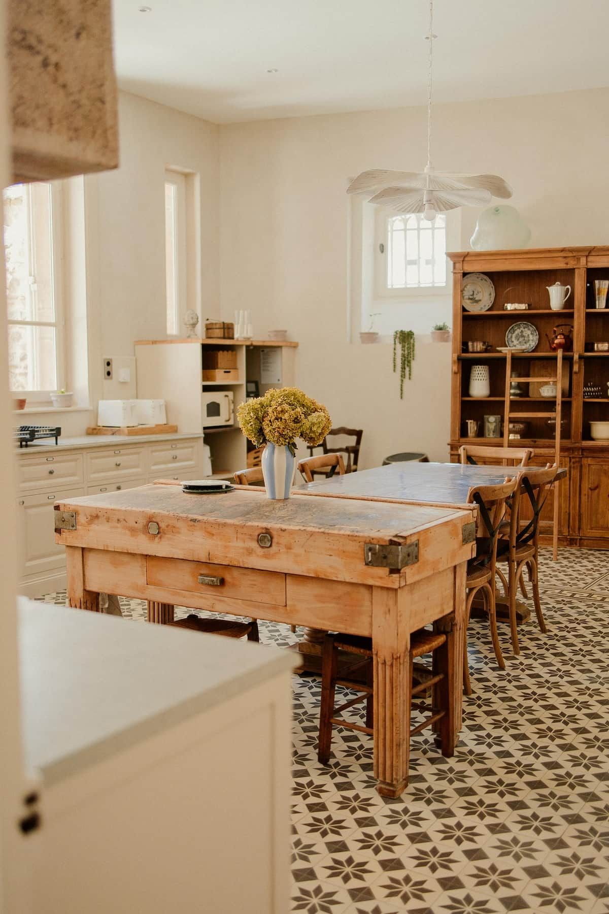 Un coin repas avec une table en bois, des chaises et un vase de fleurs. Il y a également un coin cuisine avec des placards et un luminaire suspendu.