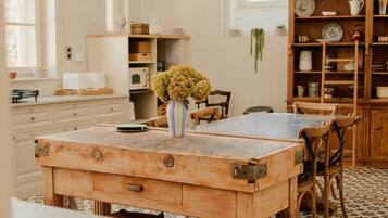Un coin repas avec une table en bois, des chaises et un vase de fleurs. Il y a également un coin cuisine avec des placards et un luminaire suspendu.