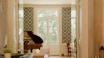 Een vleugelpiano in een ruime kamer met een groot raam, een open haard en behangpapier met een patroon.